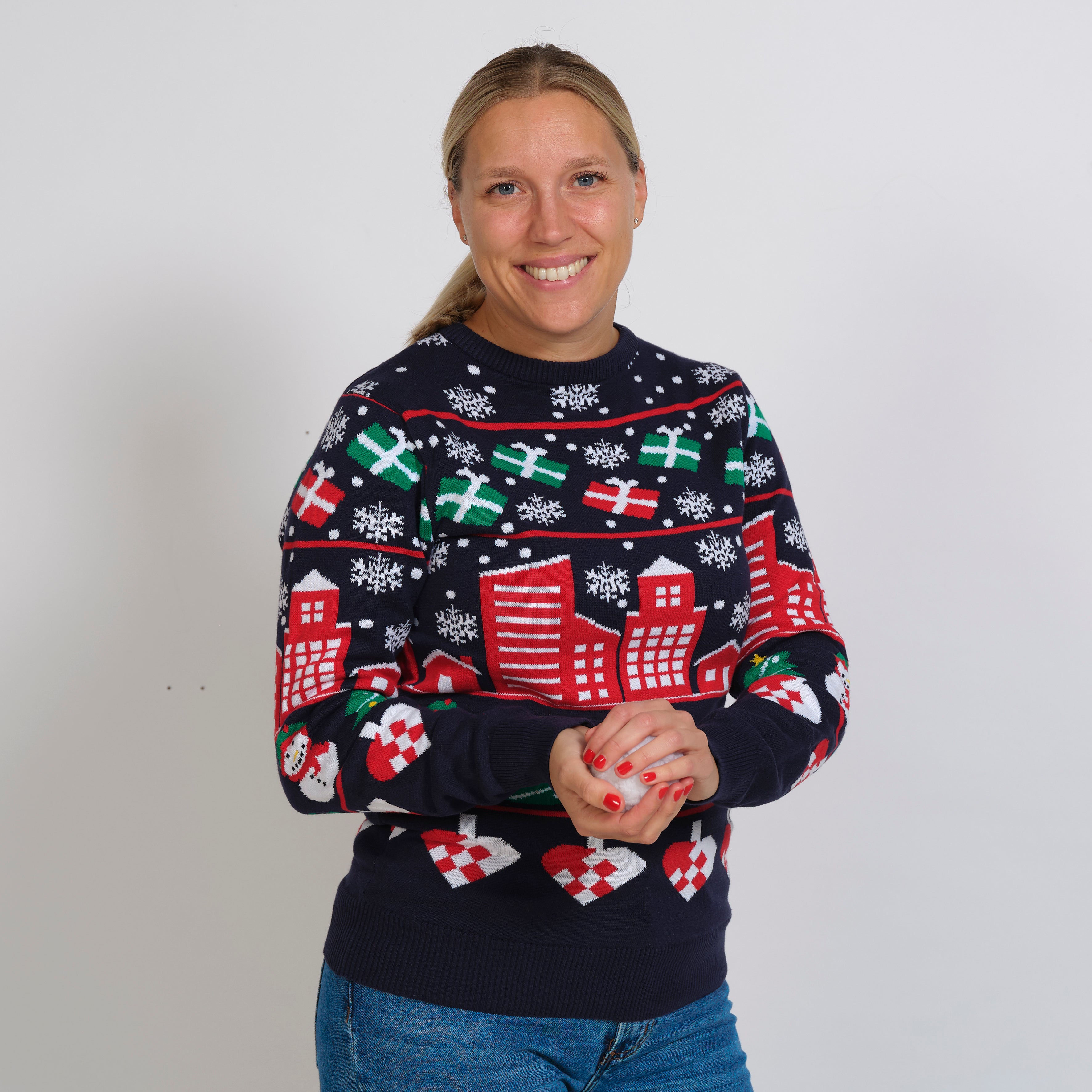 En smilende dame og en julesweater på, der har printet af en snedækket by og gaver.
